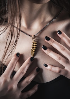 a woman with black nails holding a gold necklace