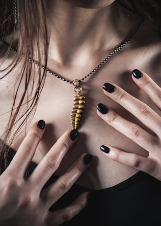 a woman with black nails holding a gold necklace