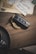 A car key fob with a luxury brand logo is placed on a wooden surface next to vintage letters with cursive handwriting and a golden spiral keychain. The letters have stamps and are partially layered on each other. A section of a dark cup and saucer is visible in the bottom left corner.