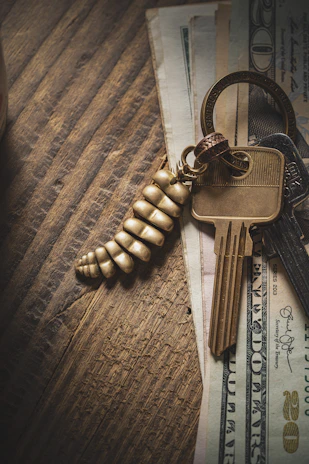 Close-up of a stack of cash on a wooden table next to house keys.