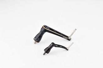 Two metallic bicycle components, including a crank arm and pedal, are placed against a plain white background. The components are sleek and streamlined with a black finish and some silver metallic elements.