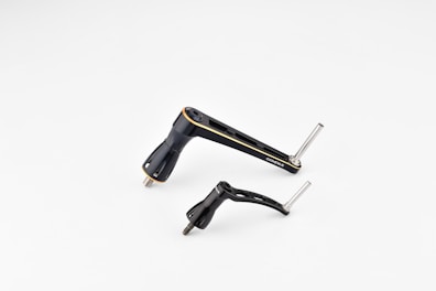 Two metallic bicycle components, including a crank arm and pedal, are placed against a plain white background. The components are sleek and streamlined with a black finish and some silver metallic elements.
