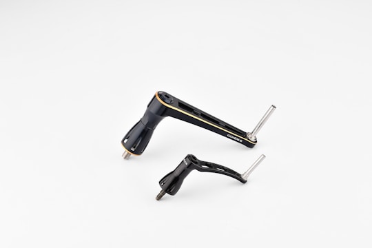 Two metallic bicycle components, including a crank arm and pedal, are placed against a plain white background. The components are sleek and streamlined with a black finish and some silver metallic elements.