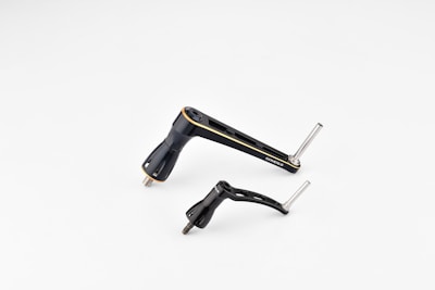 Two metallic bicycle components, including a crank arm and pedal, are placed against a plain white background. The components are sleek and streamlined with a black finish and some silver metallic elements.