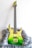 A green electric guitar with a gradient finish from yellow at the top to deep green at the bottom. It has a sleek, modern design and rests on a fluffy gray surface. The guitar features gold hardware, including the bridge and machine heads, and appears well-crafted.