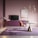 A stylish modern living room features a minimalist design with a round table with a gold-accented base, a plush pink chair, and a large purple carpet. A sleek floor lamp stands to the side, and a console with a flat-screen TV is placed against a soft pink wall. Above the setting hangs a contemporary chandelier, and a framed abstract artwork adds a touch of sophistication.