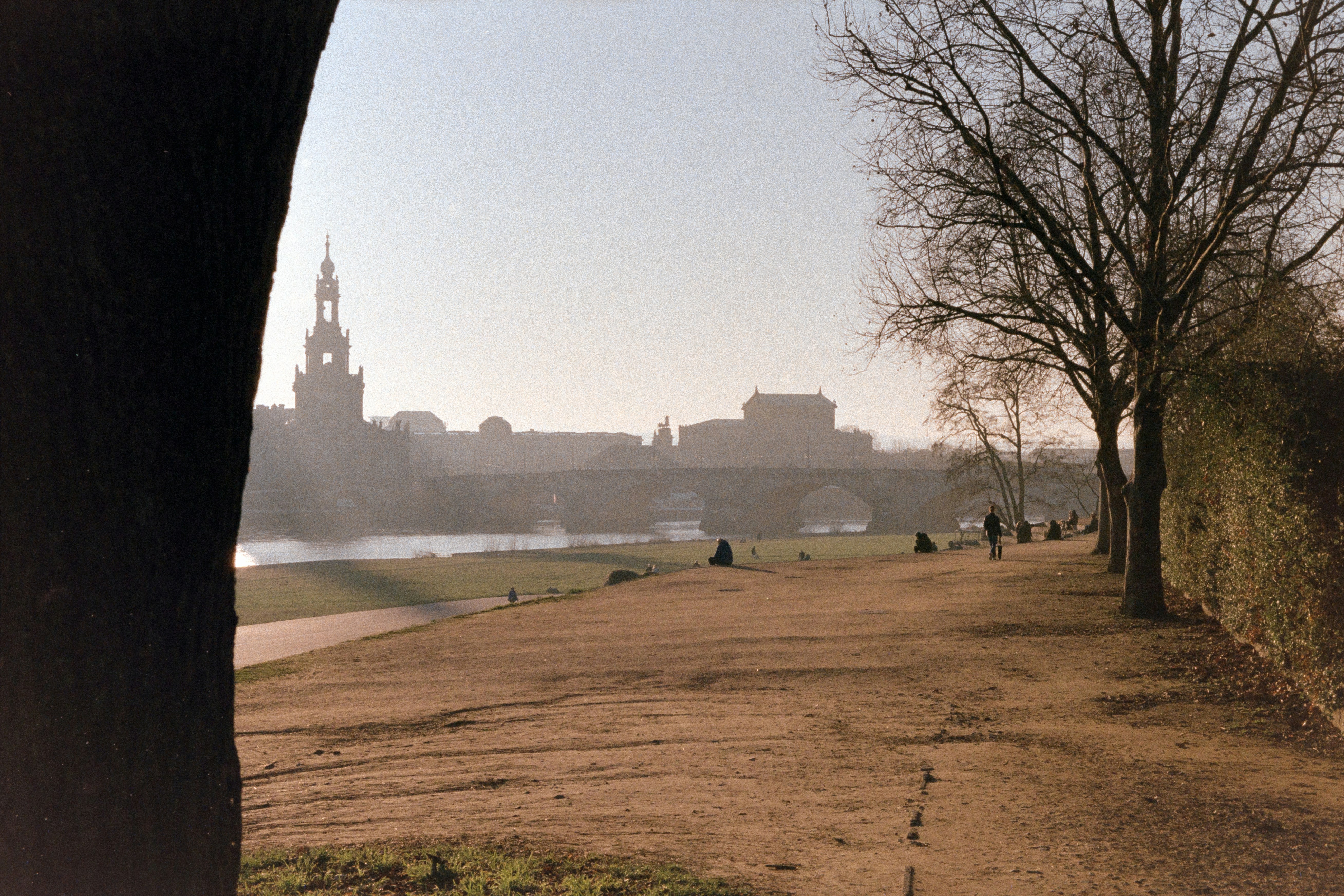 a group of people walking down a dirt road next to a river