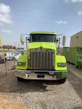 Heavy-duty tipper truck parked outside a busy industrial workshop under bright safety lights