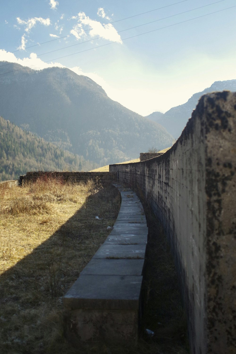 a stone wall in a field with mountains in the background