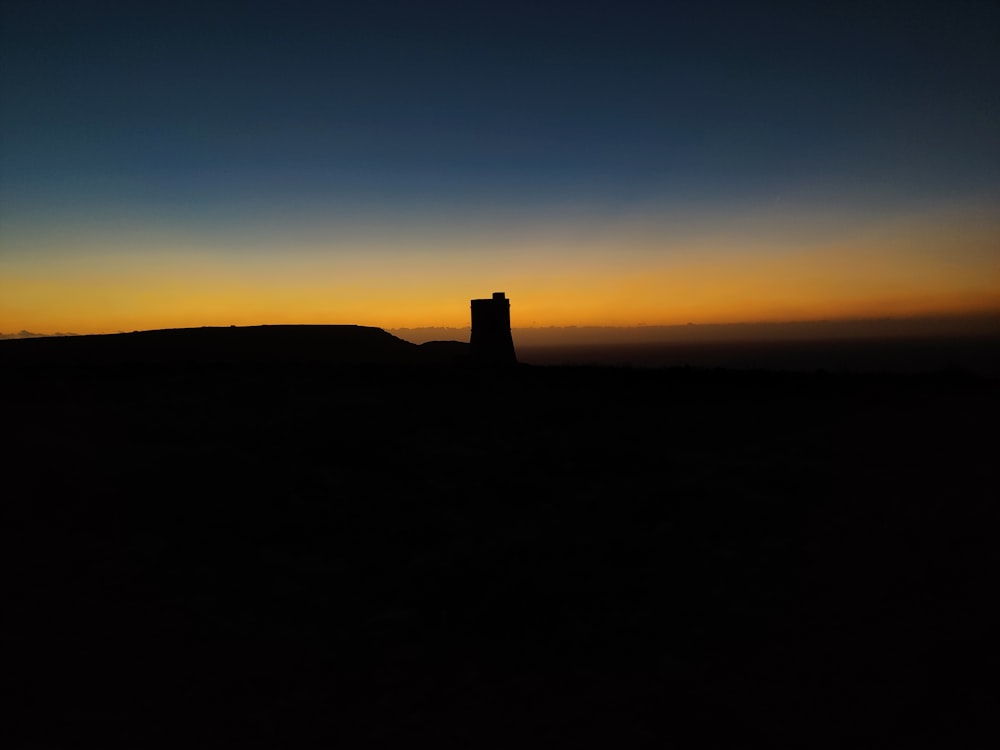 a silhouette of a tower on a hill at sunset