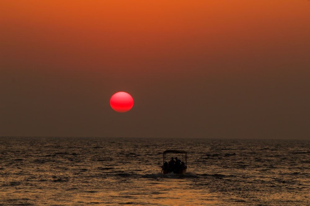 a boat in the ocean with the sun setting in the background