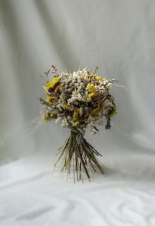 A delicate wedding bouquet of muted, dried flowers in soft blush and sage tones resting on rustic wood.