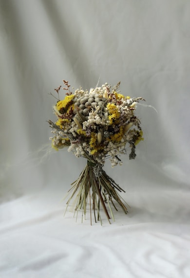 A delicate wedding bouquet of muted, dried flowers in soft blush and sage tones resting on rustic wood.