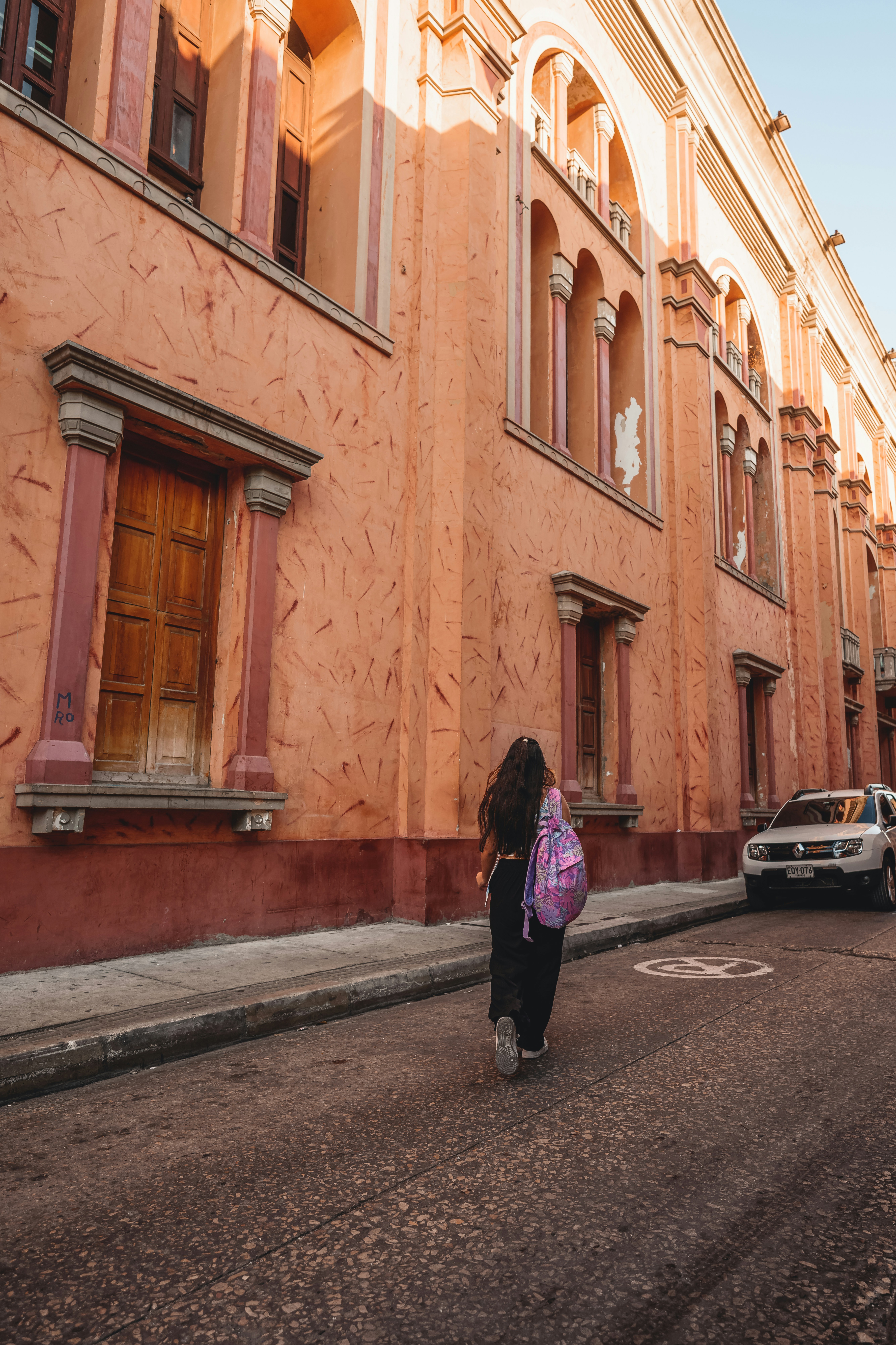 a woman walking down a street next to a tall building
