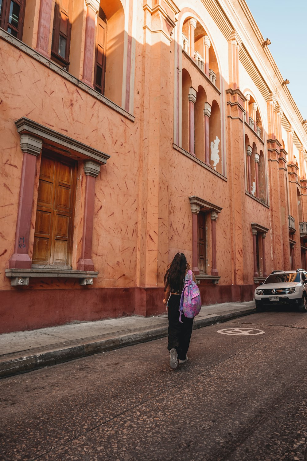 a woman walking down a street next to a tall building