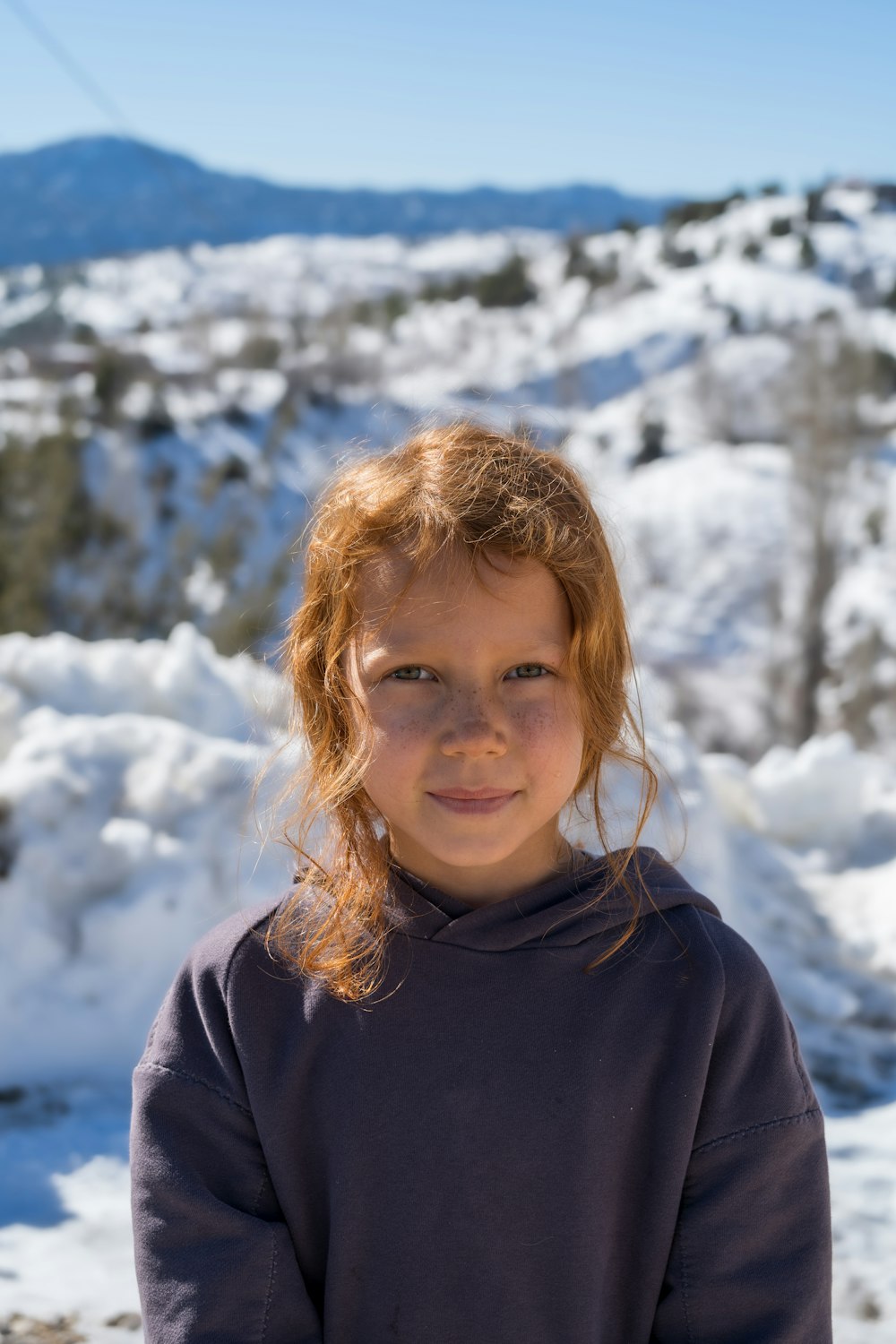 a young girl standing in the snow with a mountain in the background