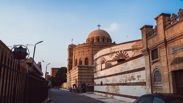 A domed brick church rising above a quiet Coptic Cairo street in warm late-afternoon light.