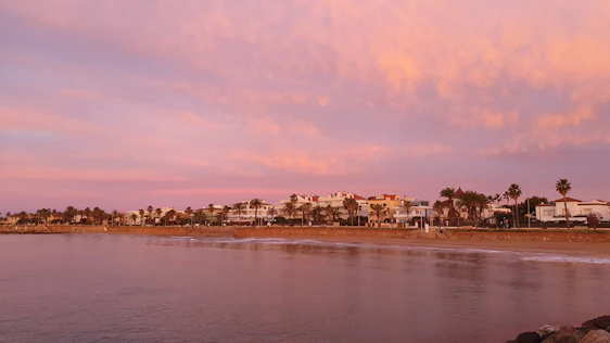Elegant coastal view of Cap Valéor with soft beige buildings and palm trees under a warm sunset.