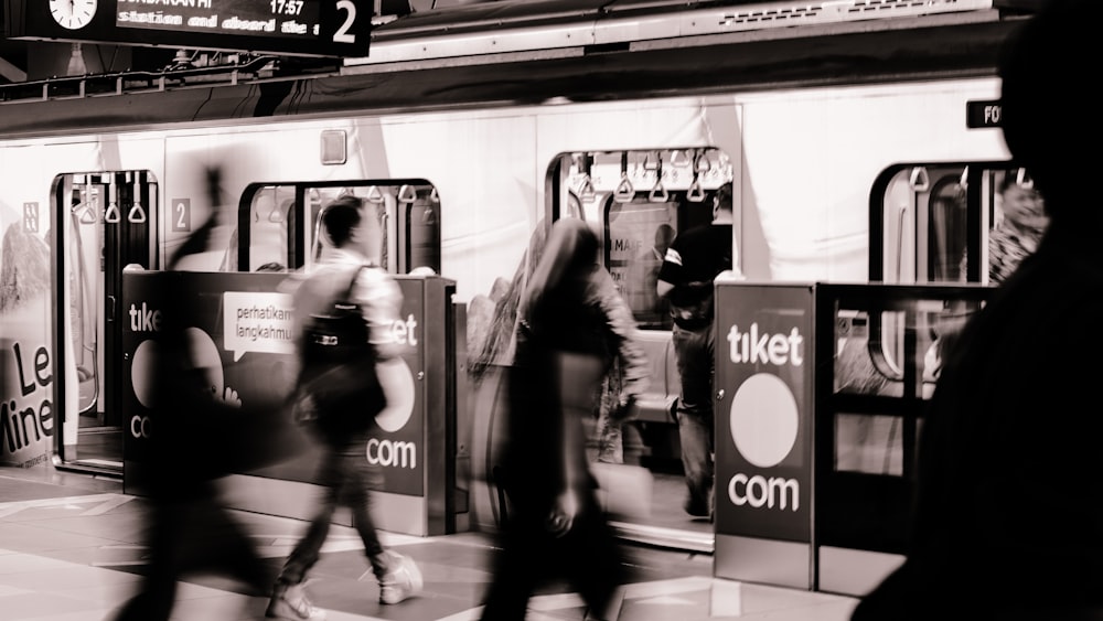 a black and white photo of people walking by a train