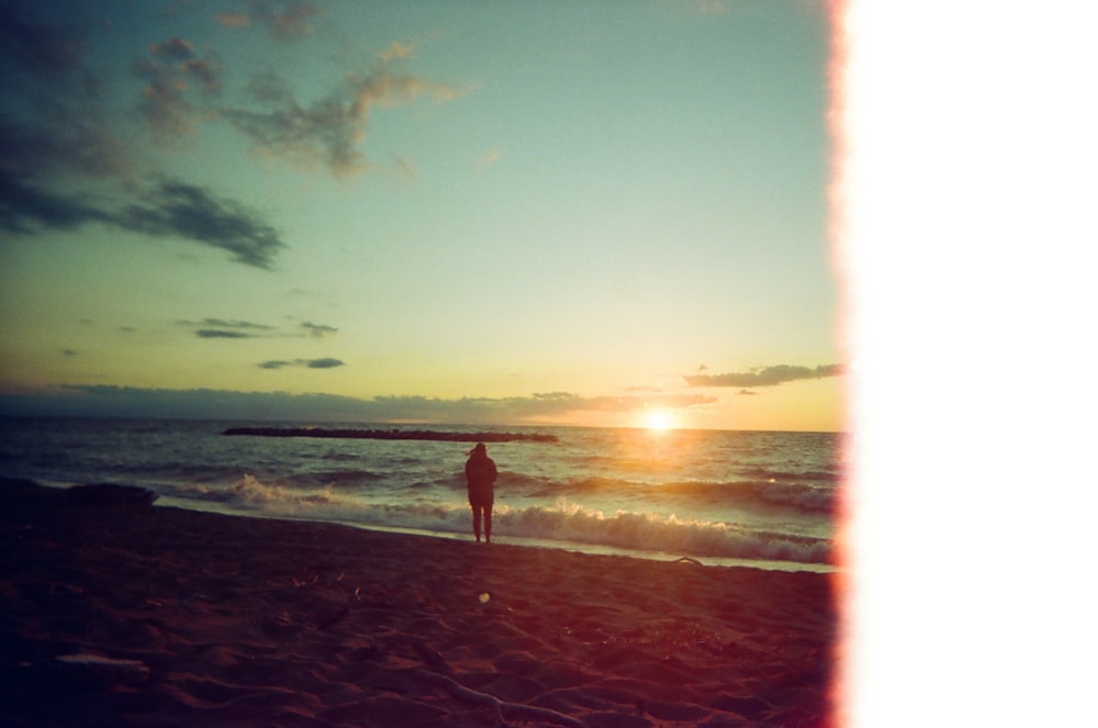 Una persona parada en una playa al atardecer