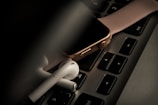 A smartwatch with a pink strap is placed on a laptop keyboard, accompanied by a pair of wireless earbuds. The scene is dimly lit, giving it a moody and tech-focused atmosphere.