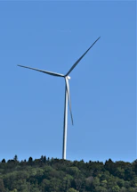 A modern wind turbine standing tall in a green rural landscape under a clear blue sky.