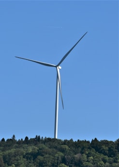 A wind turbine standing tall against a clear blue sky with green hills in the background.