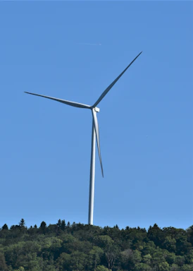 A modern wind turbine standing tall in a green rural landscape under a clear blue sky.