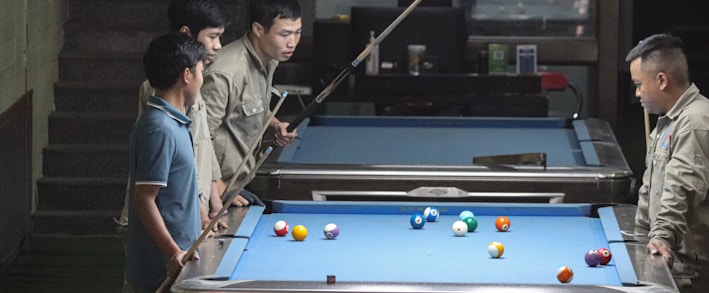 a group of men standing around a pool table