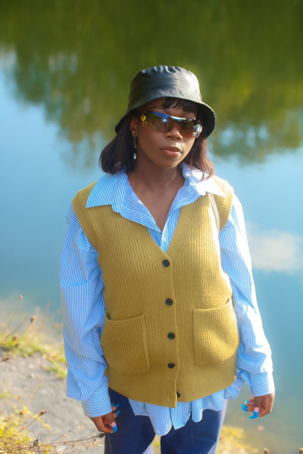 a woman wearing a hat and sunglasses standing next to a body of water