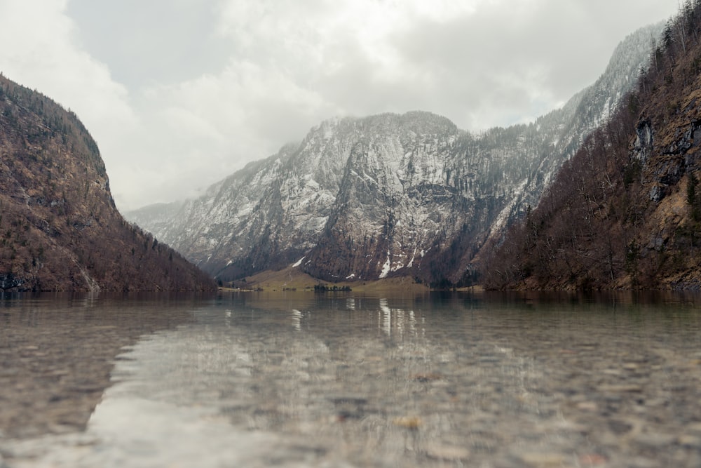 a body of water surrounded by mountains under a cloudy sky