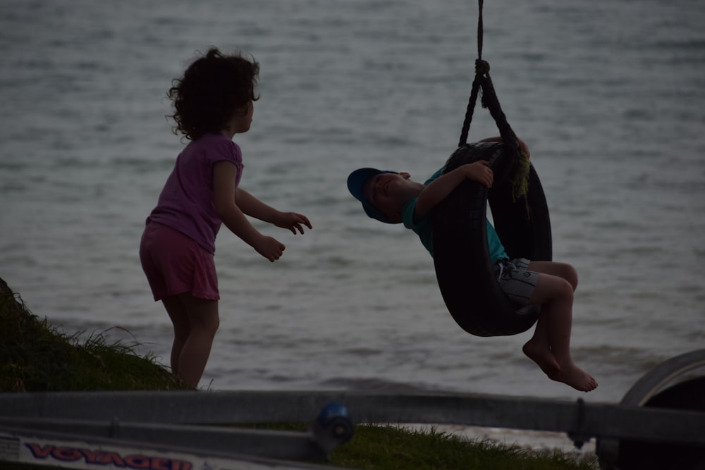 a little girl standing next to a little boy on a swing