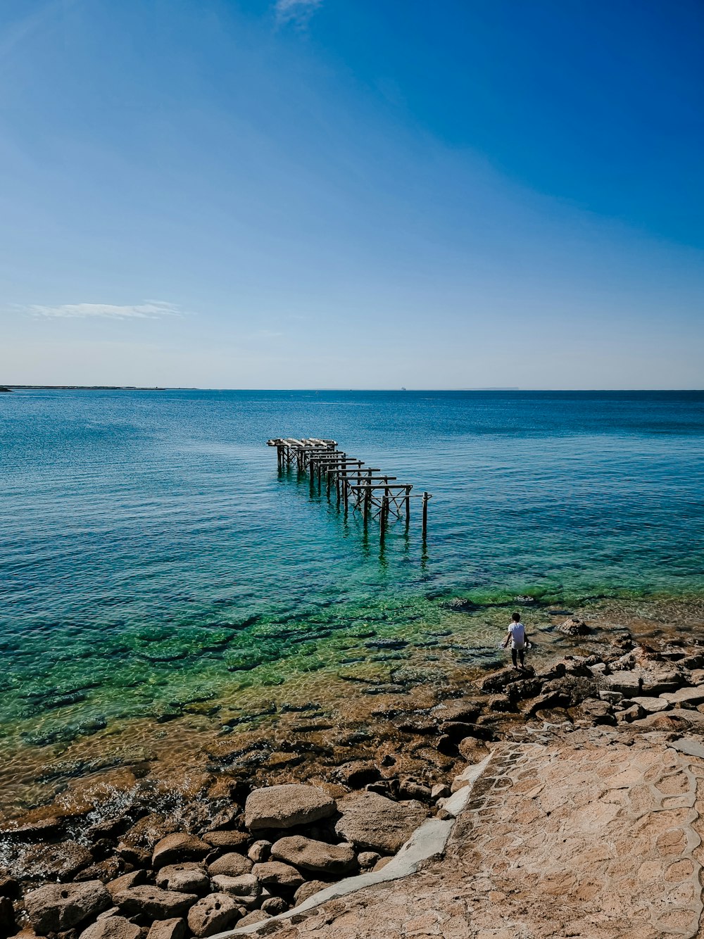 Un uomo in piedi su una spiaggia rocciosa vicino a uno specchio d'acqua