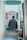 A person stands at a gas pump at a fuel station, viewed from behind. The person is wearing a jacket and appears to be refueling a vehicle. The gas pump shows numbers and has labels in what appears to be Arabic script. There are hoses and a bright orange handle visible on the pump.