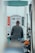A person stands at a gas pump at a fuel station, viewed from behind. The person is wearing a jacket and appears to be refueling a vehicle. The gas pump shows numbers and has labels in what appears to be Arabic script. There are hoses and a bright orange handle visible on the pump.