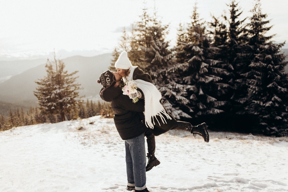 um homem segurando uma mulher em cima de uma encosta coberta de neve