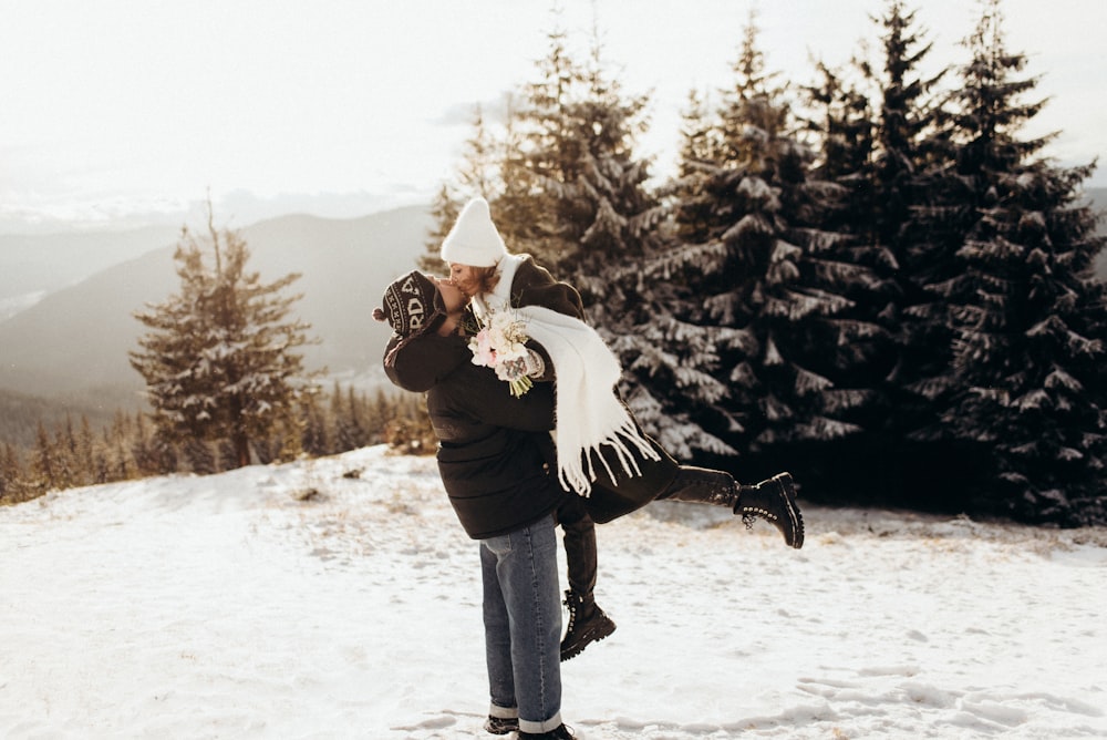 a man holding a woman on top of a snow covered slope