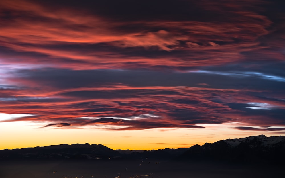 a beautiful sunset over a mountain range with clouds in the sky