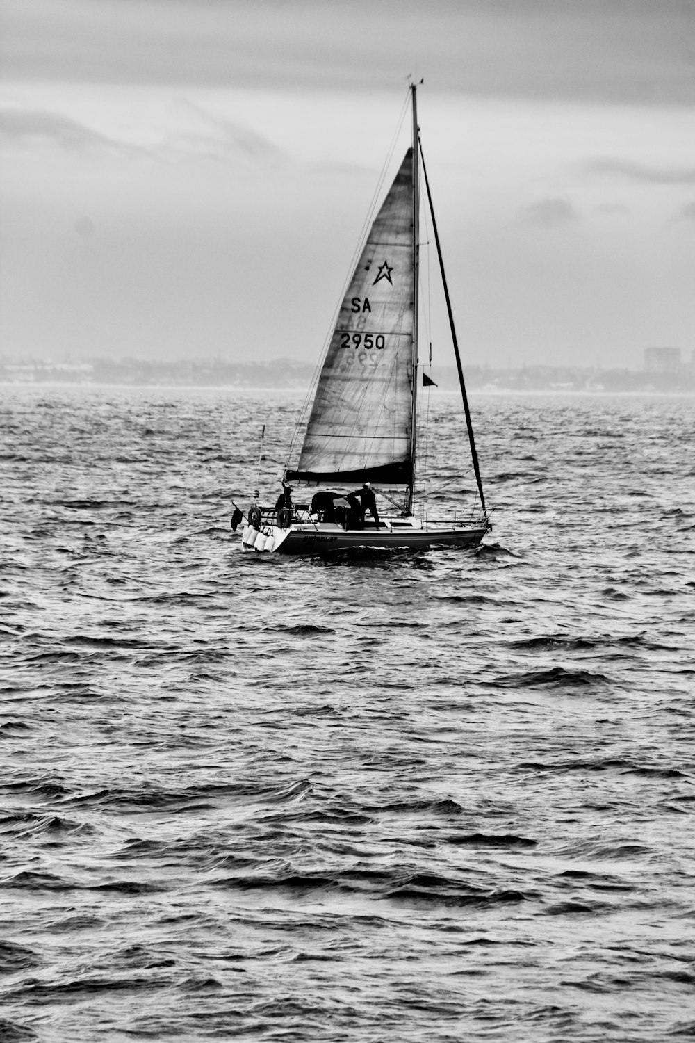 a black and white photo of a sailboat in the ocean