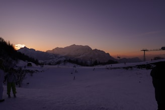 Mom skiing down a snowy slope with bright orange sunset lighting the scene.
