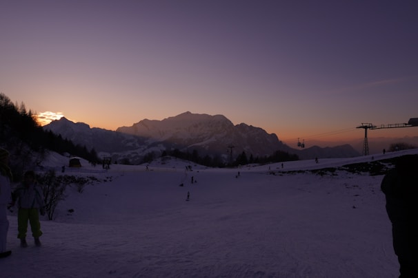 Mom skiing down a snowy slope with bright orange sunset lighting the scene.
