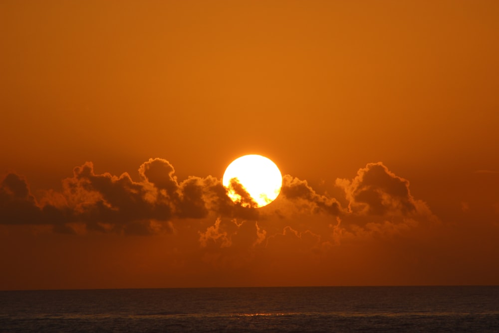 the sun is setting over the ocean with clouds