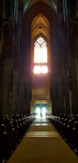 A choir singing in a sunlit church with stained glass windows.