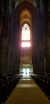 A choir singing in a sunlit church with stained glass windows.
