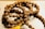 A string of prayer beads made from small, textured brown seeds, intricately arranged in a circular fashion. A yellow tassel is attached at one end, adding a vibrant touch to the earthy tones.