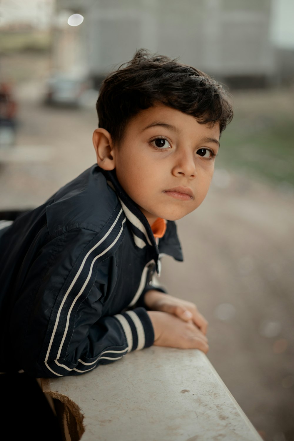 a young boy leaning on a wall looking at the camera