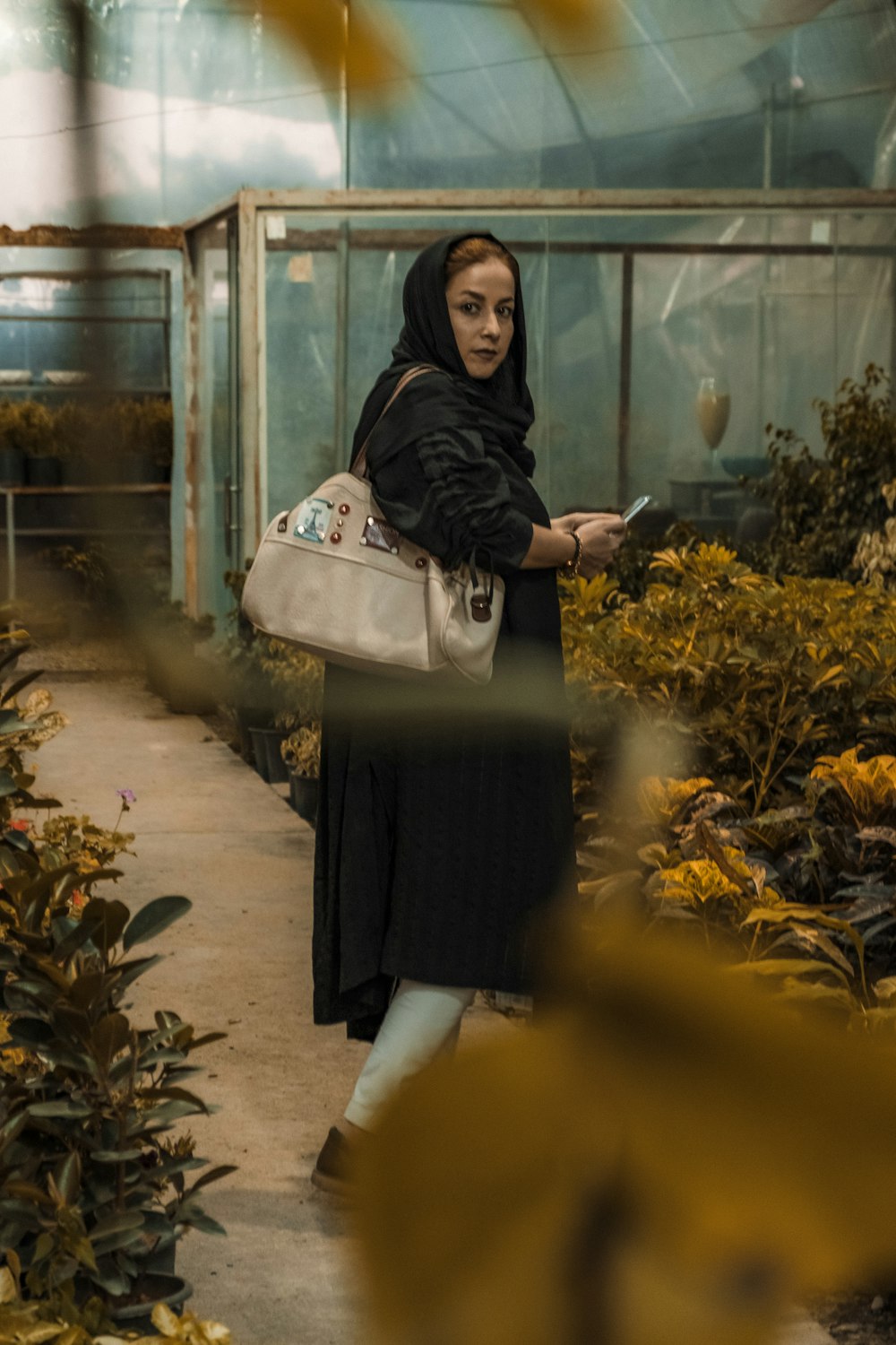 a woman standing in a greenhouse looking at her cell phone