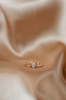 A sparkling gold ring adorned with a subtle diamond, resting on a black silk cloth.