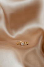 A pair of gold rings resting on a smooth, silky fabric. One of the rings features a prominent diamond, positioned centrally, adding a touch of elegance.