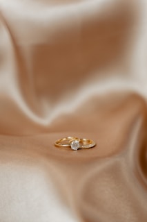 A pair of gold rings resting on a smooth, silky fabric. One of the rings features a prominent diamond, positioned centrally, adding a touch of elegance.